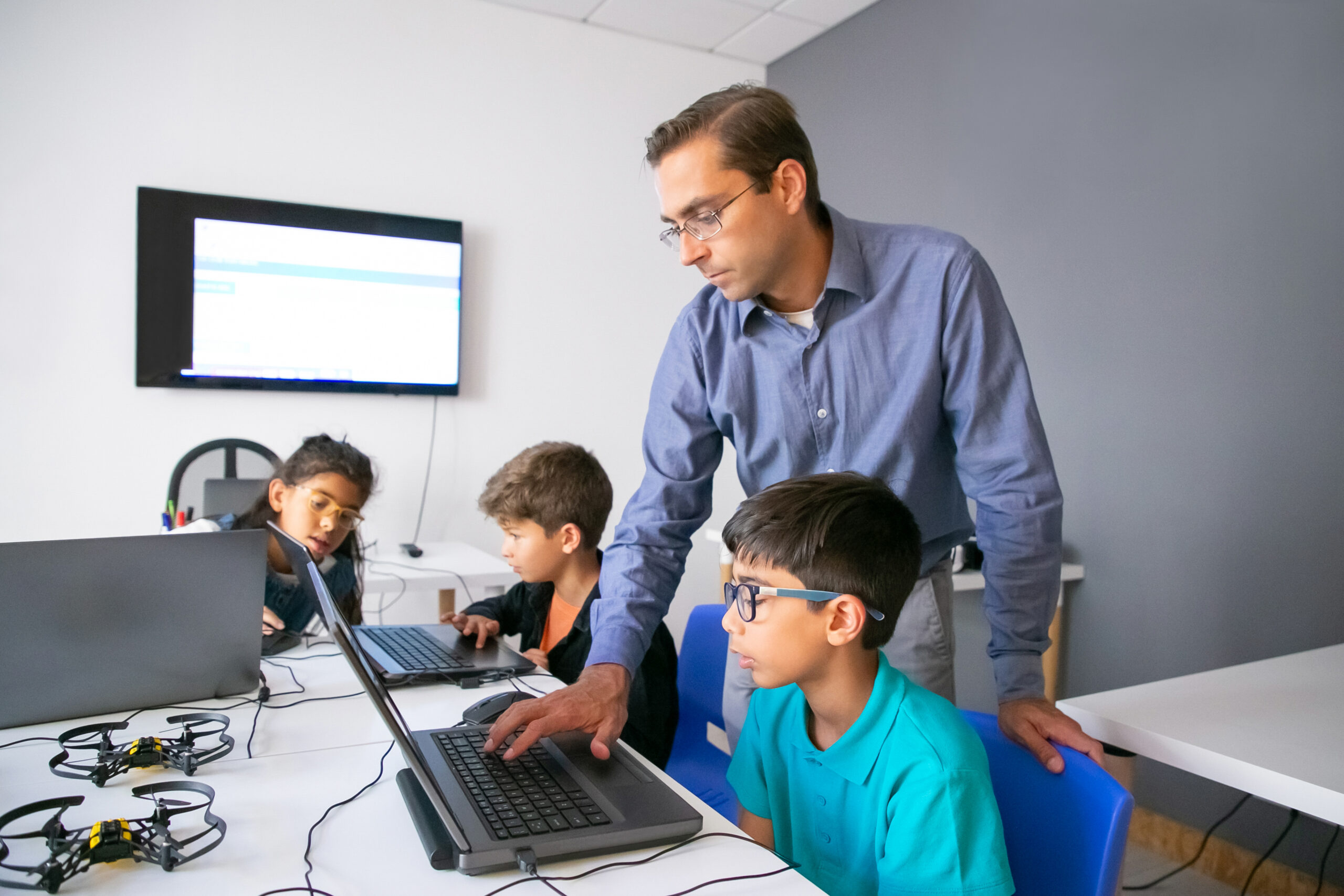 Pupils doing task on laptops and focused teacher monitoring them